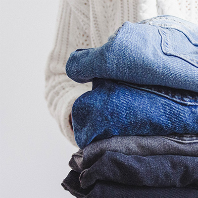 Ein Stapel gefalteter Jeans in verschiedenen Blautönen wird von einer Person in weissem Strickpullover gehalten.