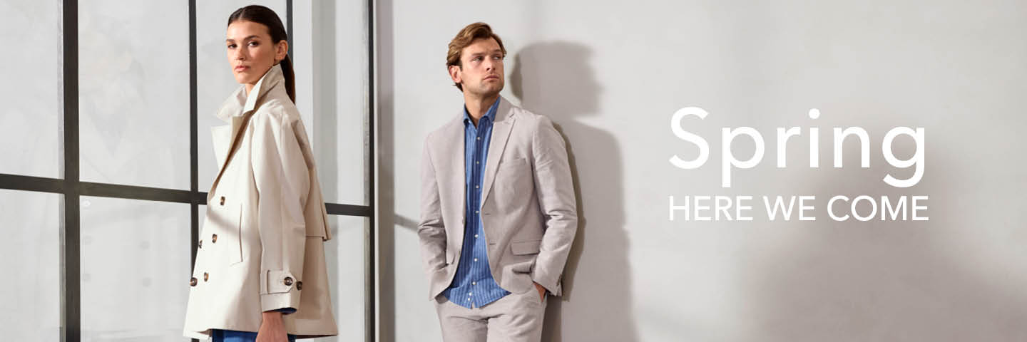 Ein Mann im grauen Anzug und blauen Hemd sowie eine Frau im hellen Mantel stehen vor einer Glasfensterfront; daneben der Text: "Spring Here We Come".