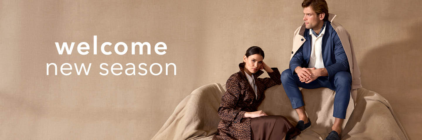 Ein Mann in einem blauen Anzug und eine Frau im Leopardenmantel sitzen auf einem hellbraunen Sofa vor einem beigen Hintergrund mit dem Text "welcome new season".