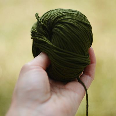 A hand holding a ball of dark green yarn.