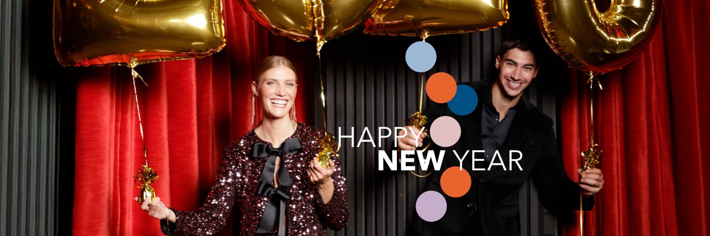 Két fiatal ember boldogan tart arany színű, számos léggömböket piros függöny előtt, "Happy New Year" felirattal a képen.