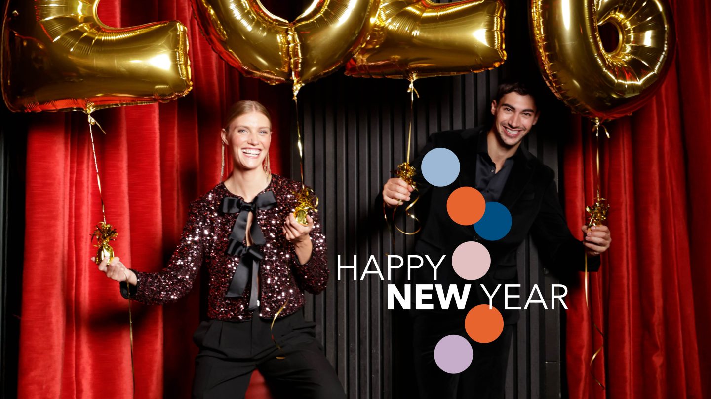 Két ember áll vörös függönyök előtt, arany színű 2024-es lufik tartva, boldogan mosolyognak. A képen színes körök láthatók, valamint a "Happy New Year" (Boldog új évet) felirat olvasható.